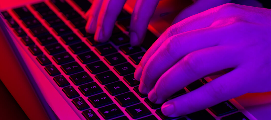 A man uses a laptop, close-up, male hands in neon lighting.